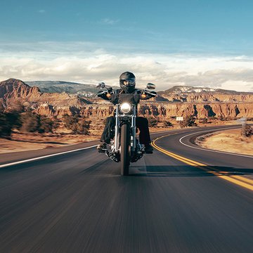 Motocicleta Cruiser sendo pilotada em uma estrada rural