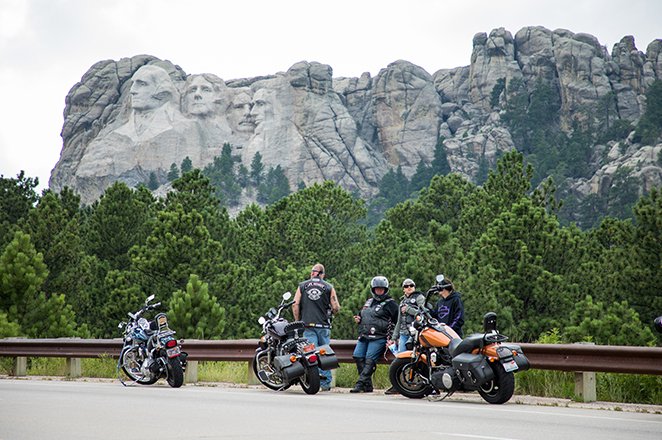 Motorcycle riders standing in front of Mount Rushmore
