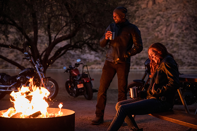 人们围坐在篝火旁，不远处停着摩托车