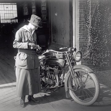 mujer junto a una motocicleta de principios del 1900