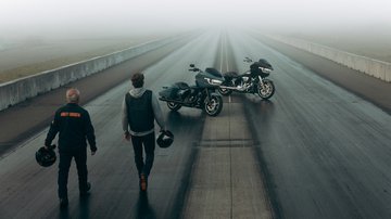 Two people walk down road to their motorcycles