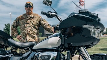 Man in camouflage military uniform stands behind motorcycle