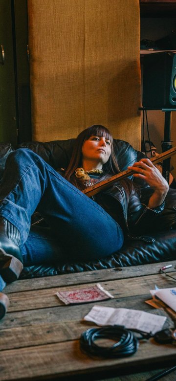 Tamara Raye Vik sits on couch as she plays the bass guitar