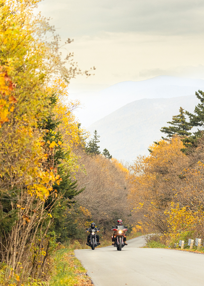 Two motorcyclists ride their bikes on scenic road