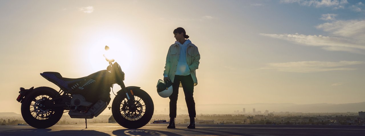 Motocykl LiveWire Del Mar při východu slunce se ženou vedle motocyklu