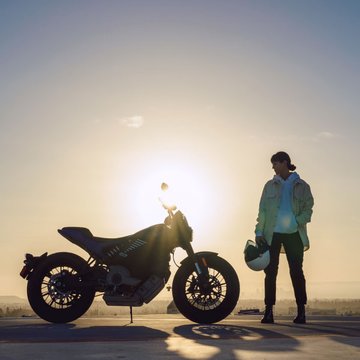 Motocykl LiveWire Del Mar při východu slunce se ženou vedle motocyklu