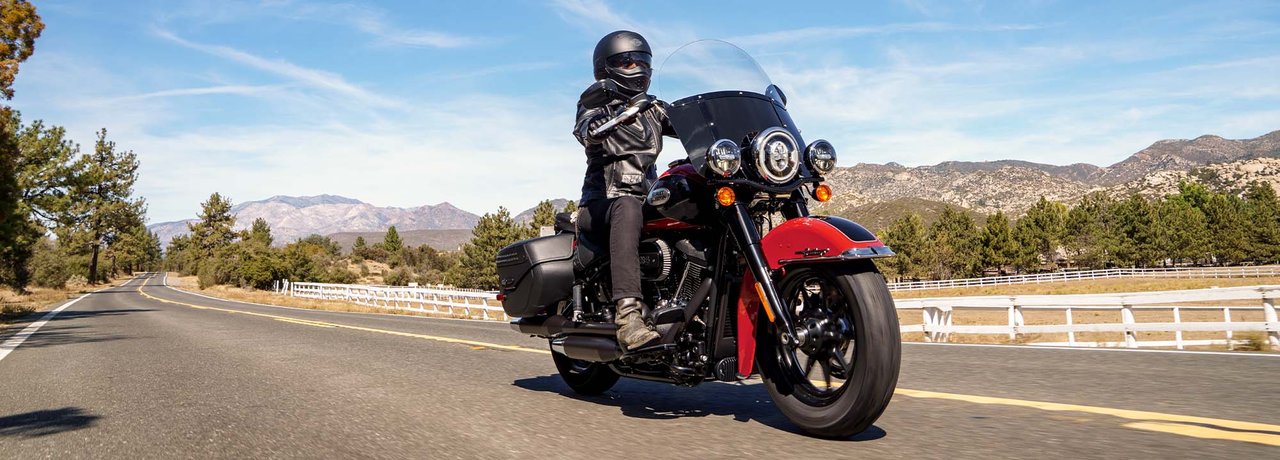 Vue de trois quarts avant d’un pilote en équipement Harley noir à pleine vitesse sur un modèle Heritage Classic 2022, photographié sur une route dans le désert