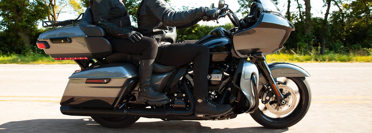 Motociclista vestindo roupas para pilotar Harley pretas pilotando em alta velocidade uma Road Glide Limited 2022 na cor Billiard Red em uma estrada nas montanhas.
