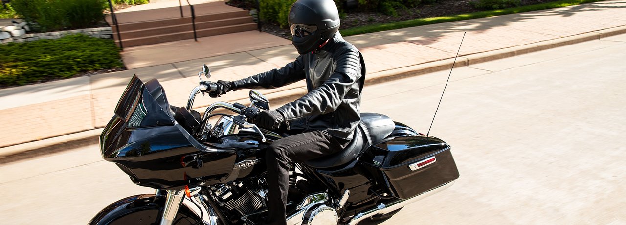 Side profile of driver in black Harley gear speeding 2022 Road Glide in Vivid Black against blurred background