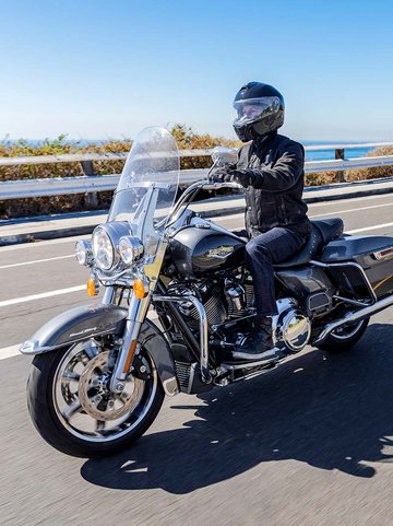 Motociclista con indosso l’equipaggiamento Harley in nero mentre guida una Road King 2022 color Vivid Black lungo una strada campestre