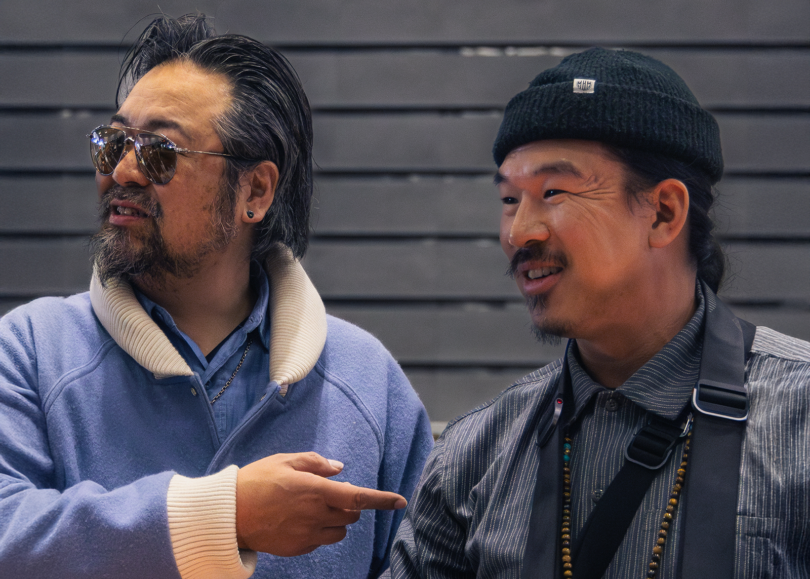 A man wearing chrome aviator sunglasses points to his left at David Chang as they pose for a picture
