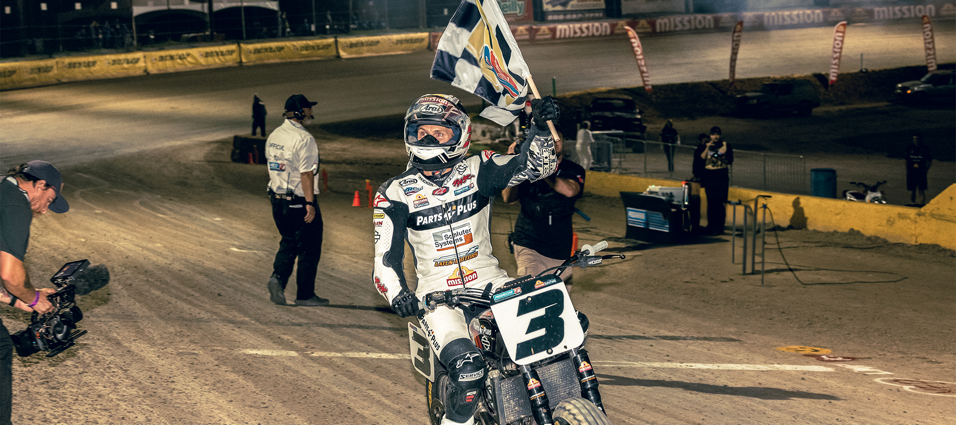 Briar Bauman carries a checkered flag as he circles a dirt track after winning a race