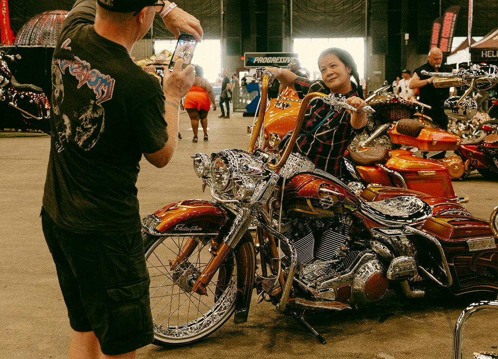 Close view of custom motorcycles parked together while attendees gather and take photos around them.