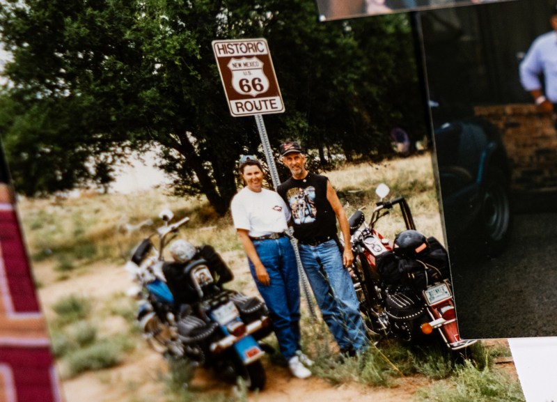 Vintage photo of two people standing beside parked motorcycles beneath a Historic Route 66 road sign