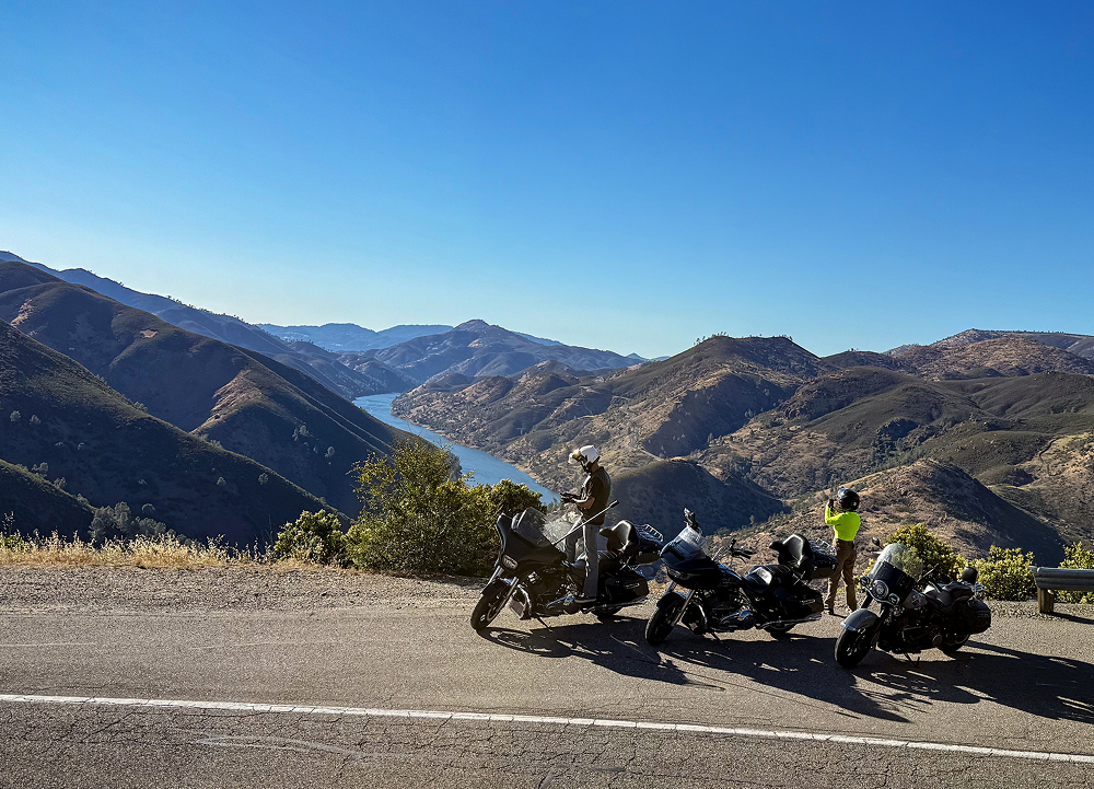 Three Harley-Davidson motorcycles overlook a winding river canyon as riders stop at a scenic mountain vista