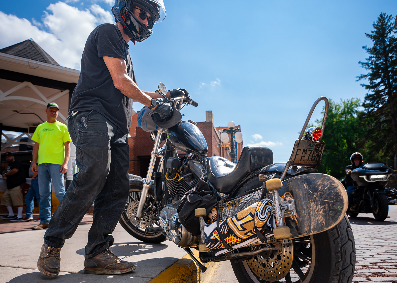 A skateboard and pool towel are strapped to the back of a chopper 