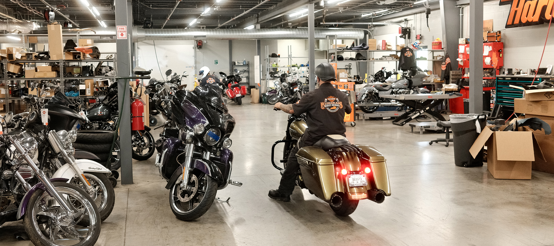 Motorcycles fill a Harley-Davidson service department as a rider moves through repair bays and workstations