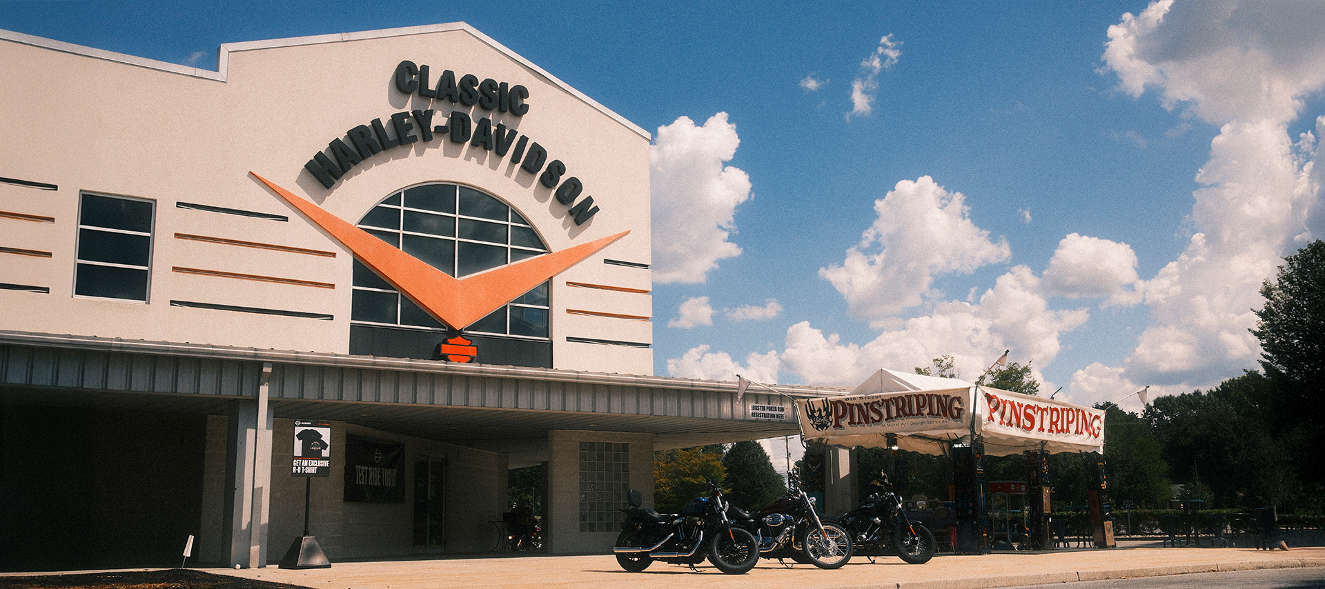 Exterior of Classic Harley-Davidson in, with motorcycles parked and a pinstriping tent outside.