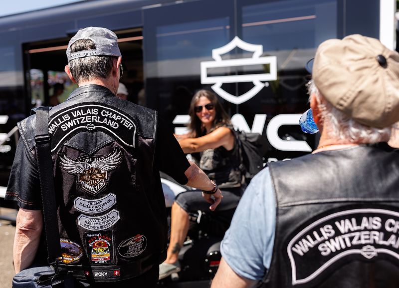 Harley-Davidson riders wearing Wallis Valais Chapter Switzerland H.O.G. patches gather outside a branded display