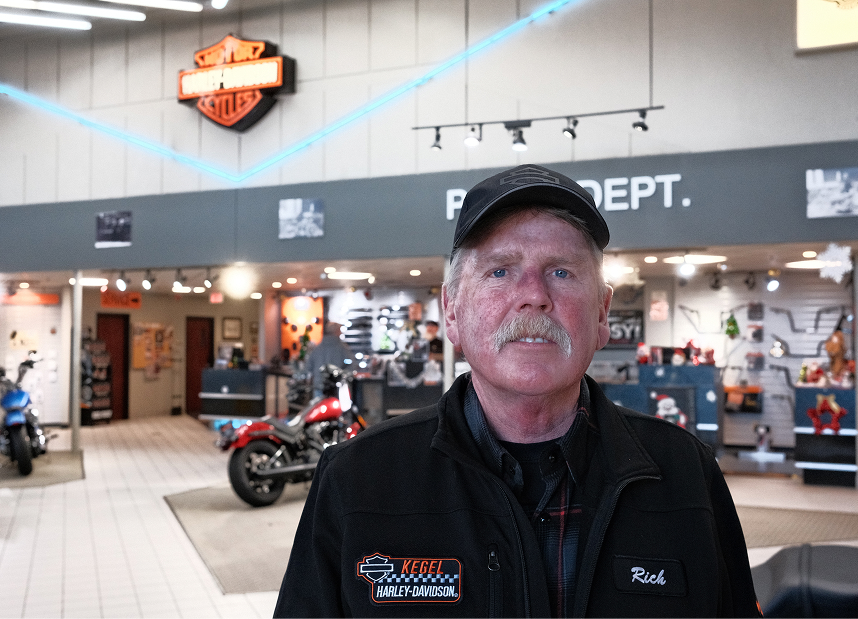 An employee with a grey moustache poses for a photo in the showroom of Kegel Harley-Davidson