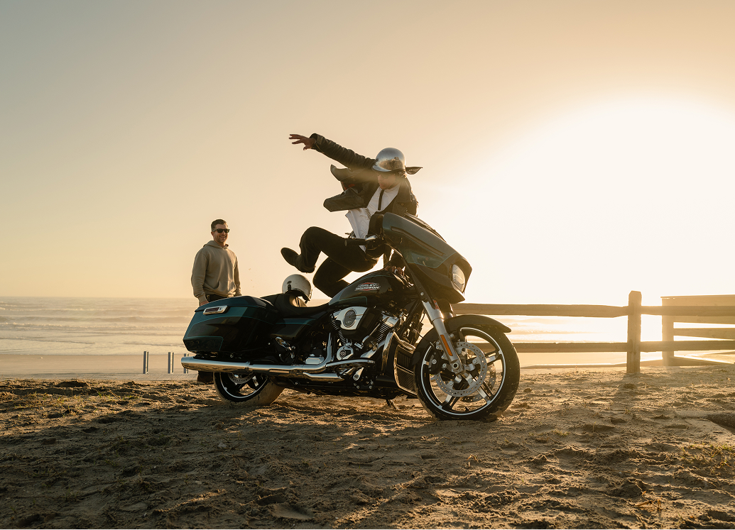 Motorcycle parked on Daytona Beach at sunset as a rider jumps over the bike near a wooden fence