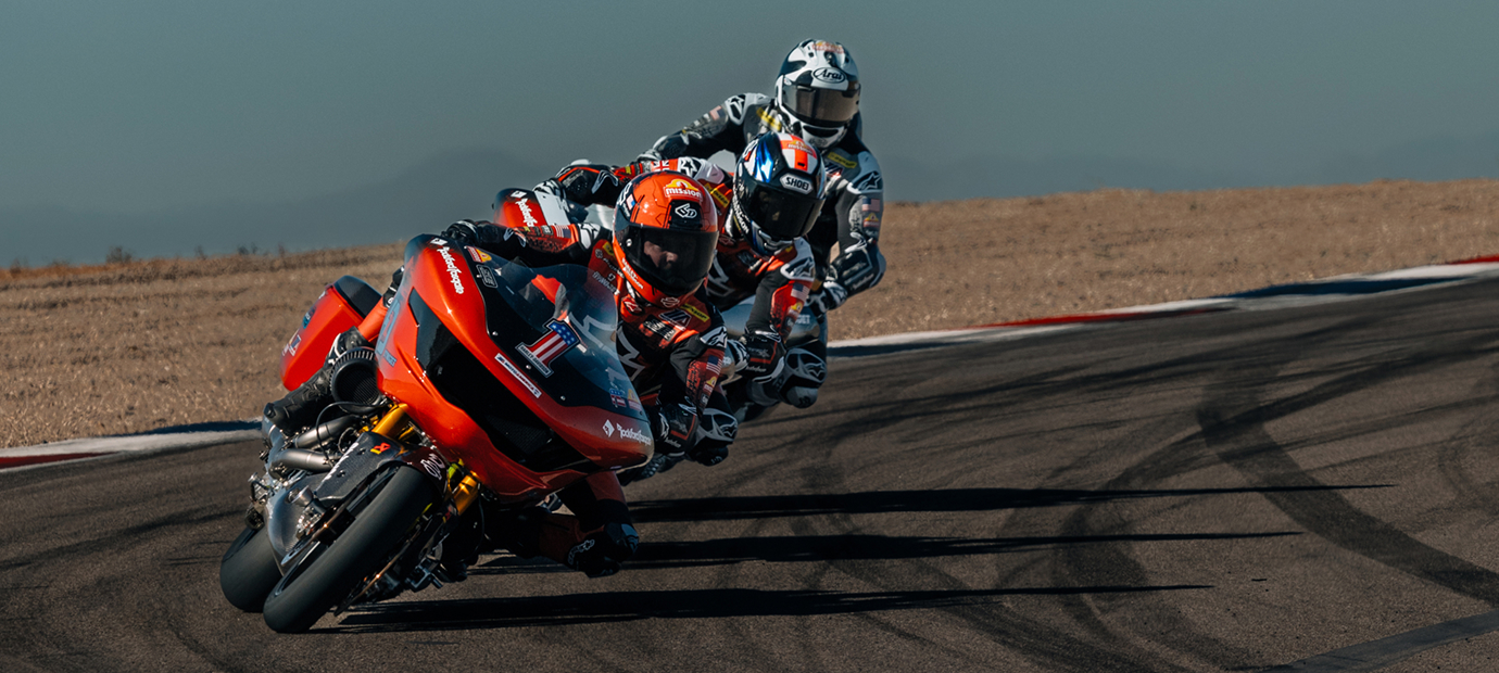 Three motorcycle racers lean tightly into a fast corner on a racetrack, riding closely in a competitive pack
