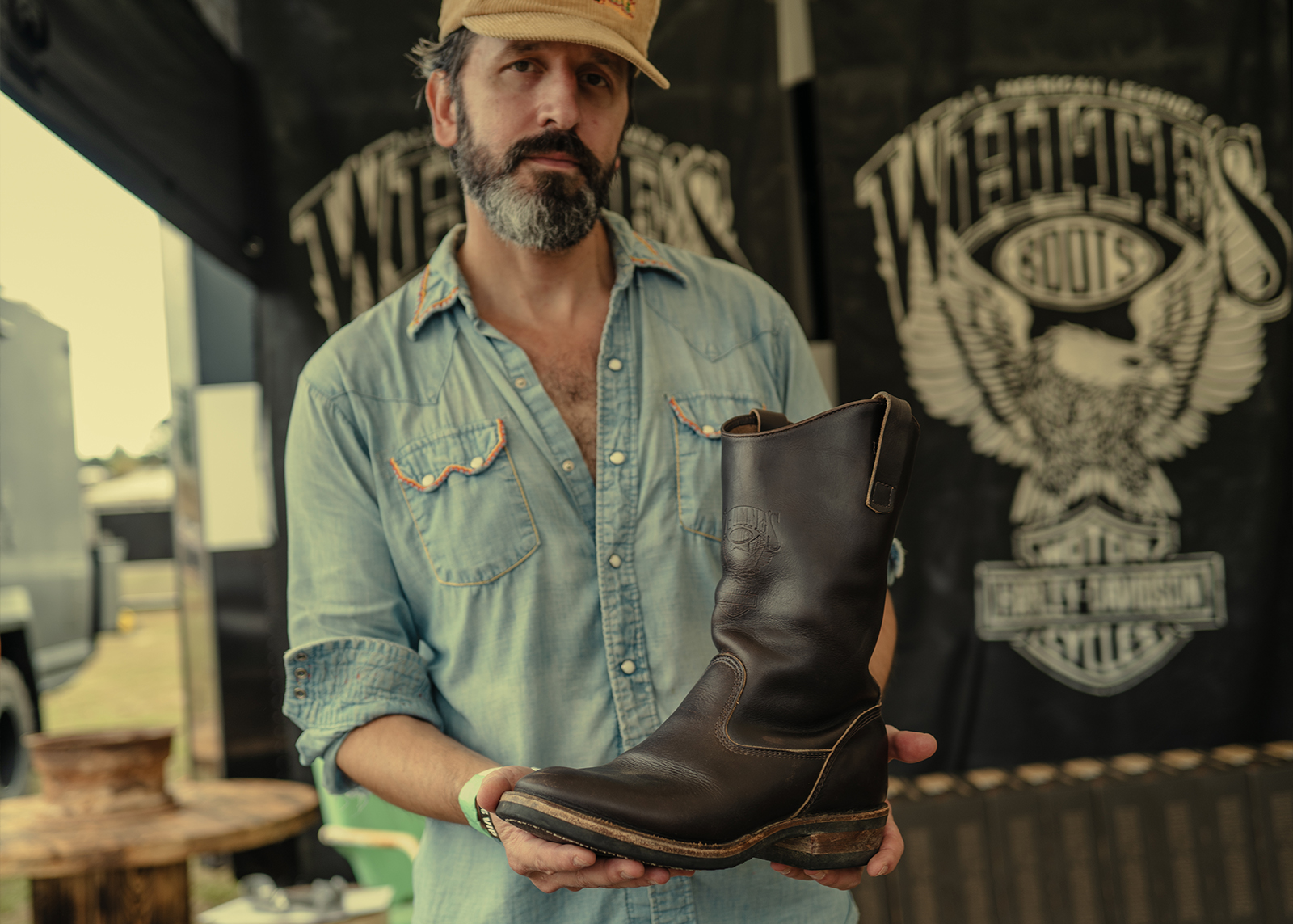 A man in a denim shirt displays a brown leather Harley-Davidson x White’s motorcycle boot.