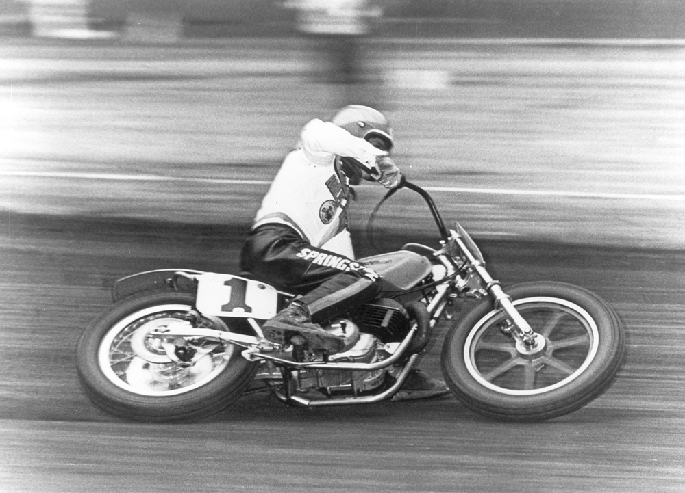 Jay Springsteen leans a Harley-Davidson motorcycle through a turn at speed with motion blur in the background