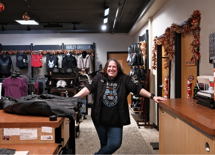 Employee leaning on a retail counter inside Harley‑Davidson of Madison store, with apparel racks and merchandise displayed behind