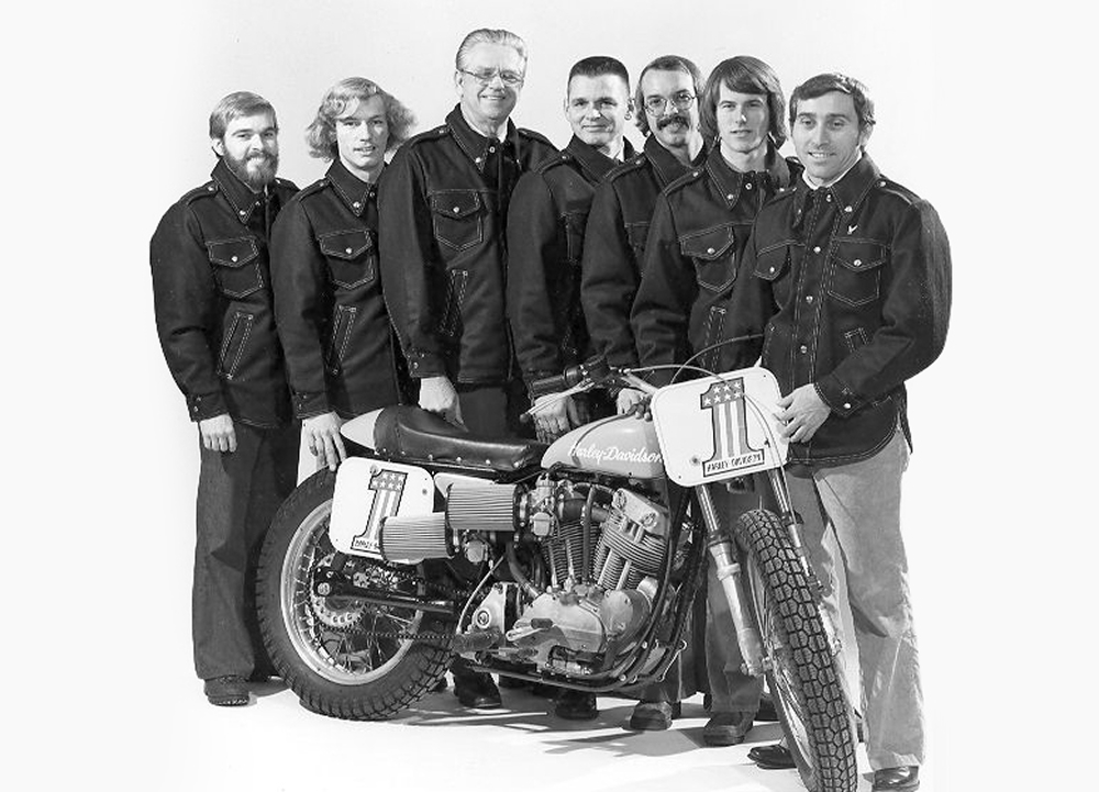 Black-and-white team portrait with crew members posing behind a number 1 Harley-Davidson flat track motorcycle