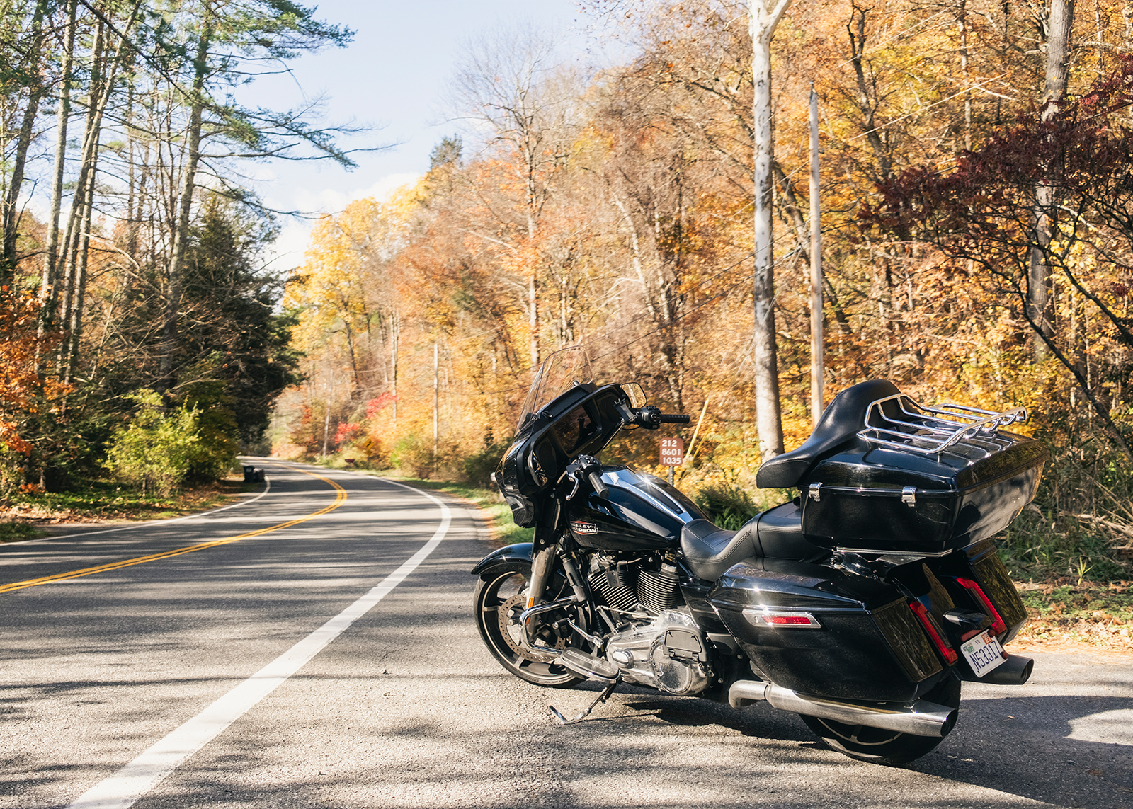 The author’s Harley-Davidson parked on the sie of a two-lane road surrounded by yellow and orange fall foliage.