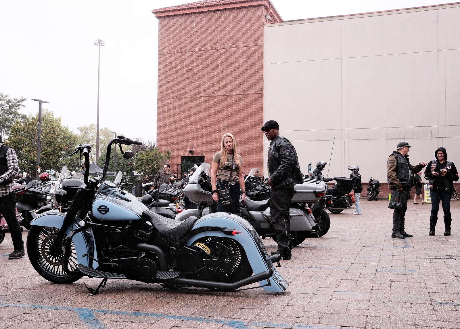Light-blue custom Harley-Davidson motorcycle parked as two people stand nearby in rainy conditions.