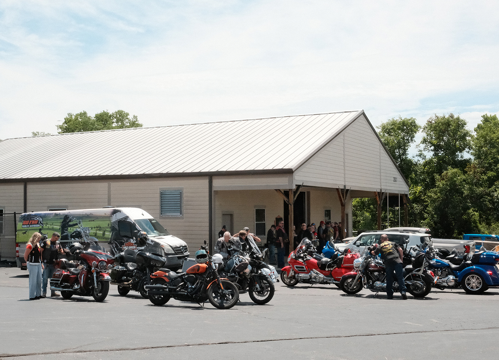 Motorcycles and riders gather outside a Man O’ War Harley-Davidson event building on a sunny day