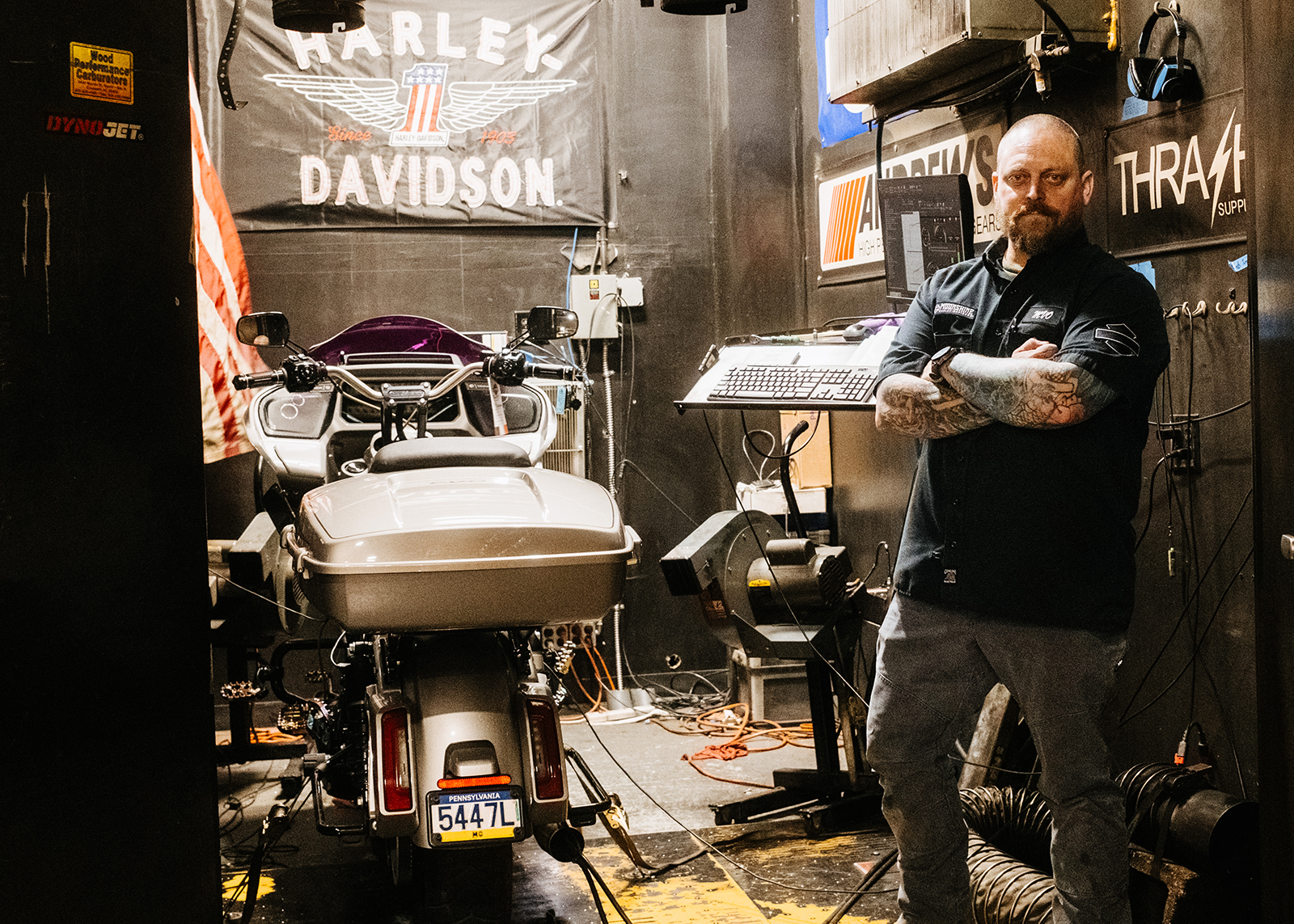 Moonshine Harley-Davidson Service and Operations Manager Mike Van Orden stands with his tattooed arms crossed looking at the camera in Moonshine’s soundproof dyno room.
