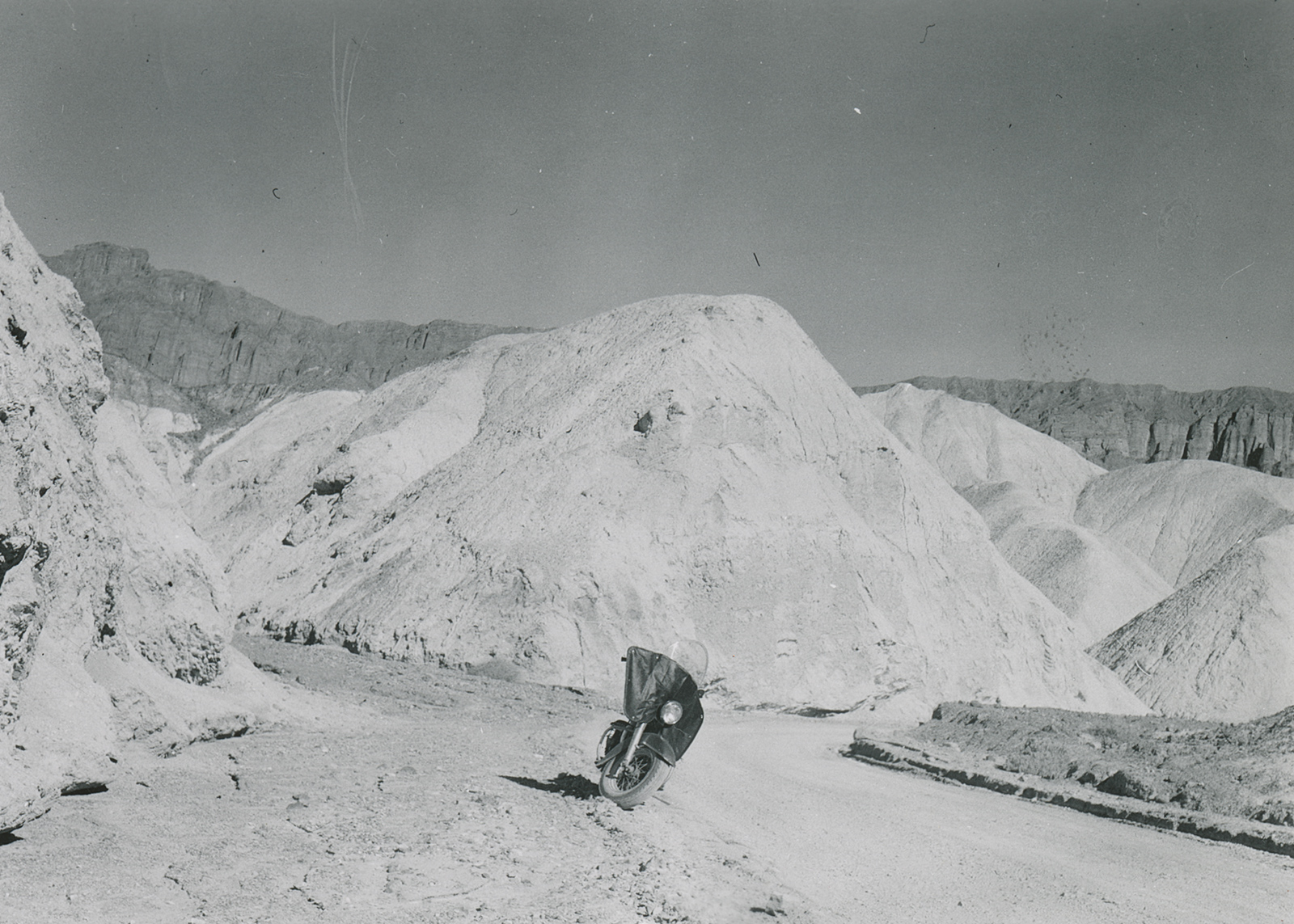 Black-and-white historical photo taken by Eldred Harrington of his 1951 hydra-glide in front of large sand formations.