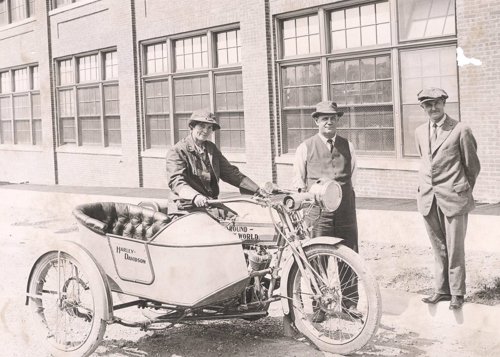 three people stand outside around a motorcycle and sidecar
