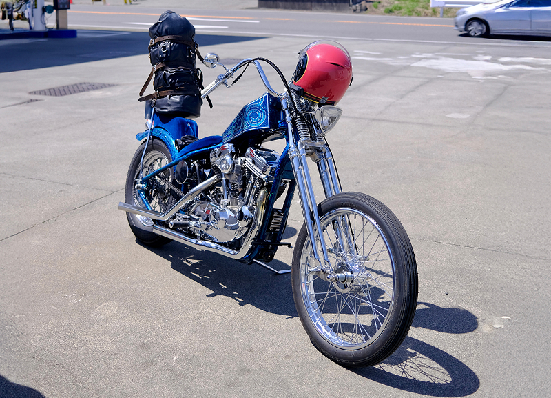 Custom chopper parked on an open paved lot with a helmet resting on the seat and minimal surroundings