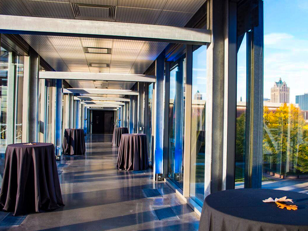 Glass-walled hallway with cocktail tables and city skyline view