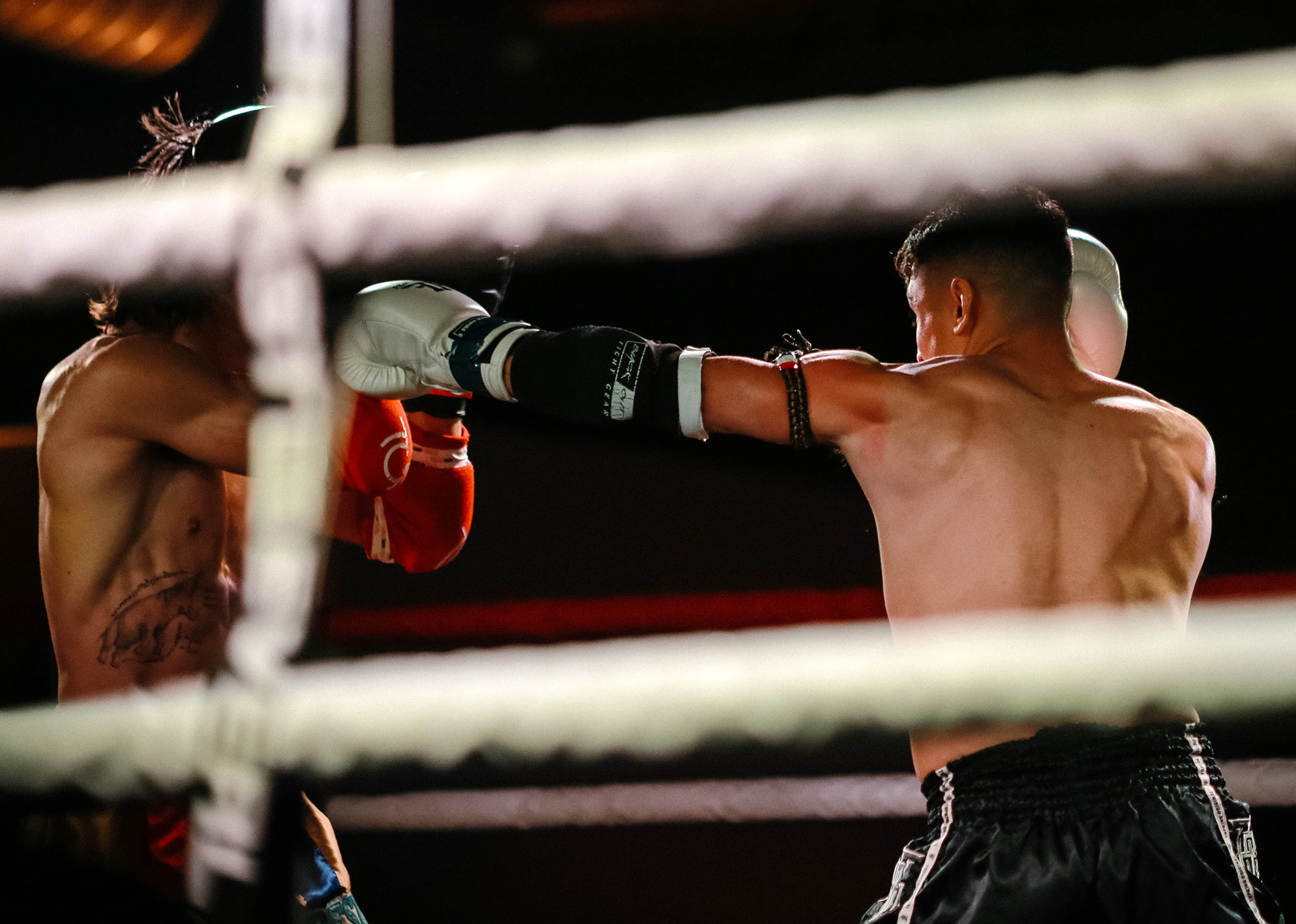 Fighter in black trunks lands a straight punch on opponent in red gloves during an intense fight.