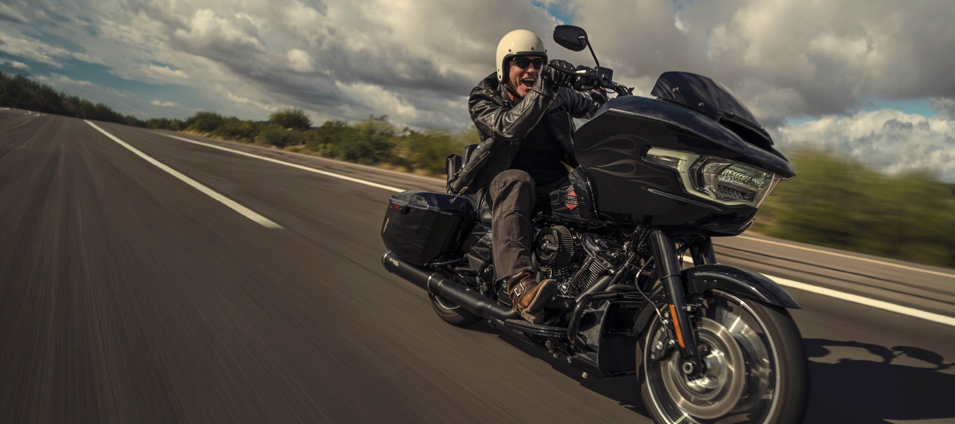 Smiling rider on a black touring motorcycle traveling at speed on an open highway.