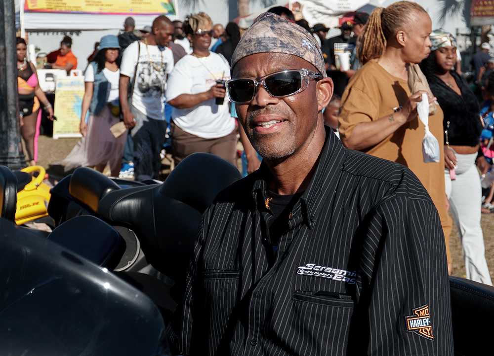 Person standing beside a parked motorcycle at a busy outdoor motorcycle gathering with people behind