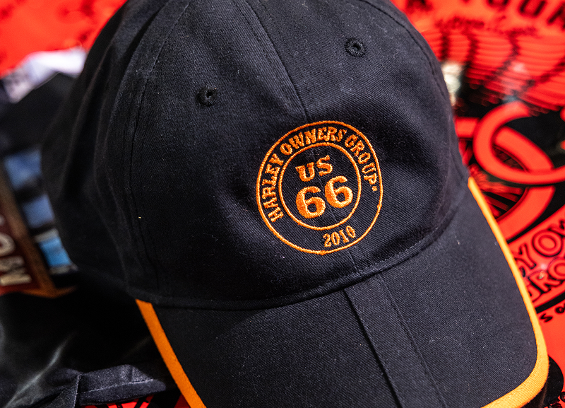 Black cap with embroidered Route 66 Harley Owners Group 2010 logo resting on a red signed banner
