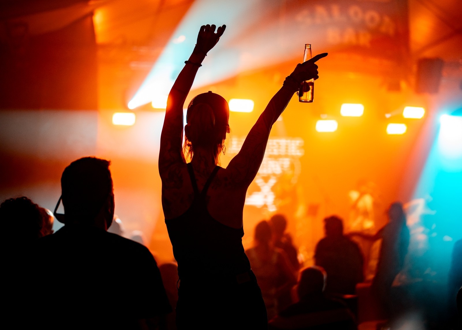A woman enjoying live music at an event, seen from behind under colorful stage lights.