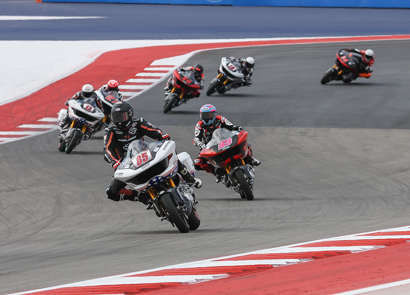 Pack of motorcycle racers lean in unison through a corner during a high-speed race