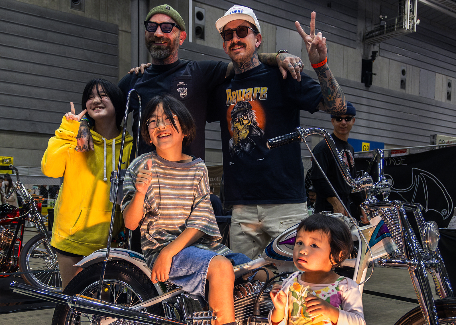 A group of adults and children smile, flash peace signs and pose with a custom chopper
