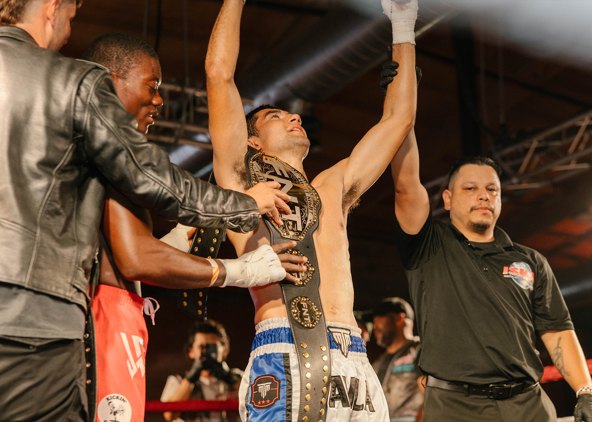 Fighter Ruben Avila raises arms in victory as he is awarded a championship belt inside the ring after the fight.