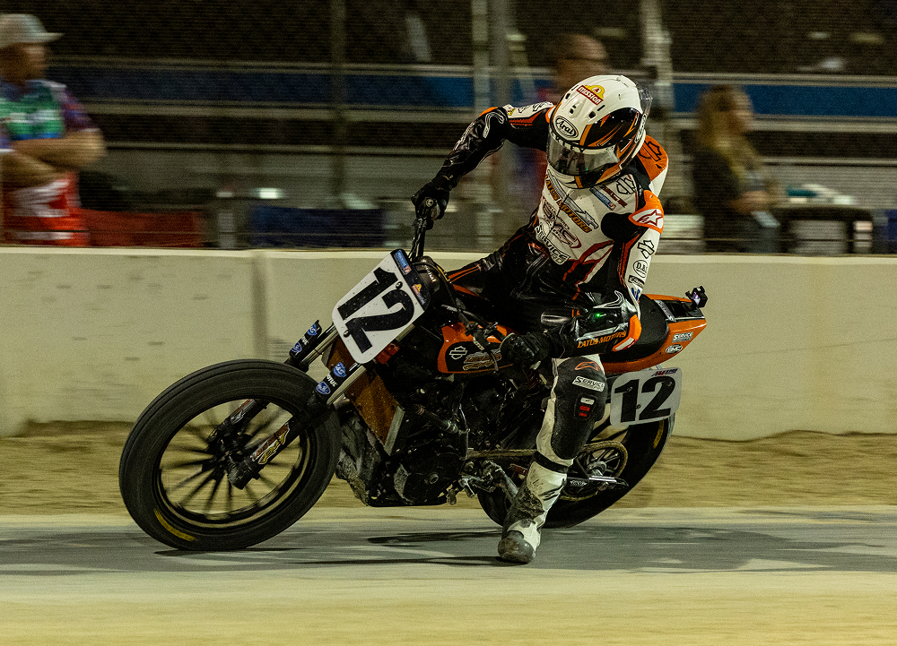 Flat track rider Kody Kopp leans into a dirt-track corner during a nighttime race, kicking up dust under stadium lights