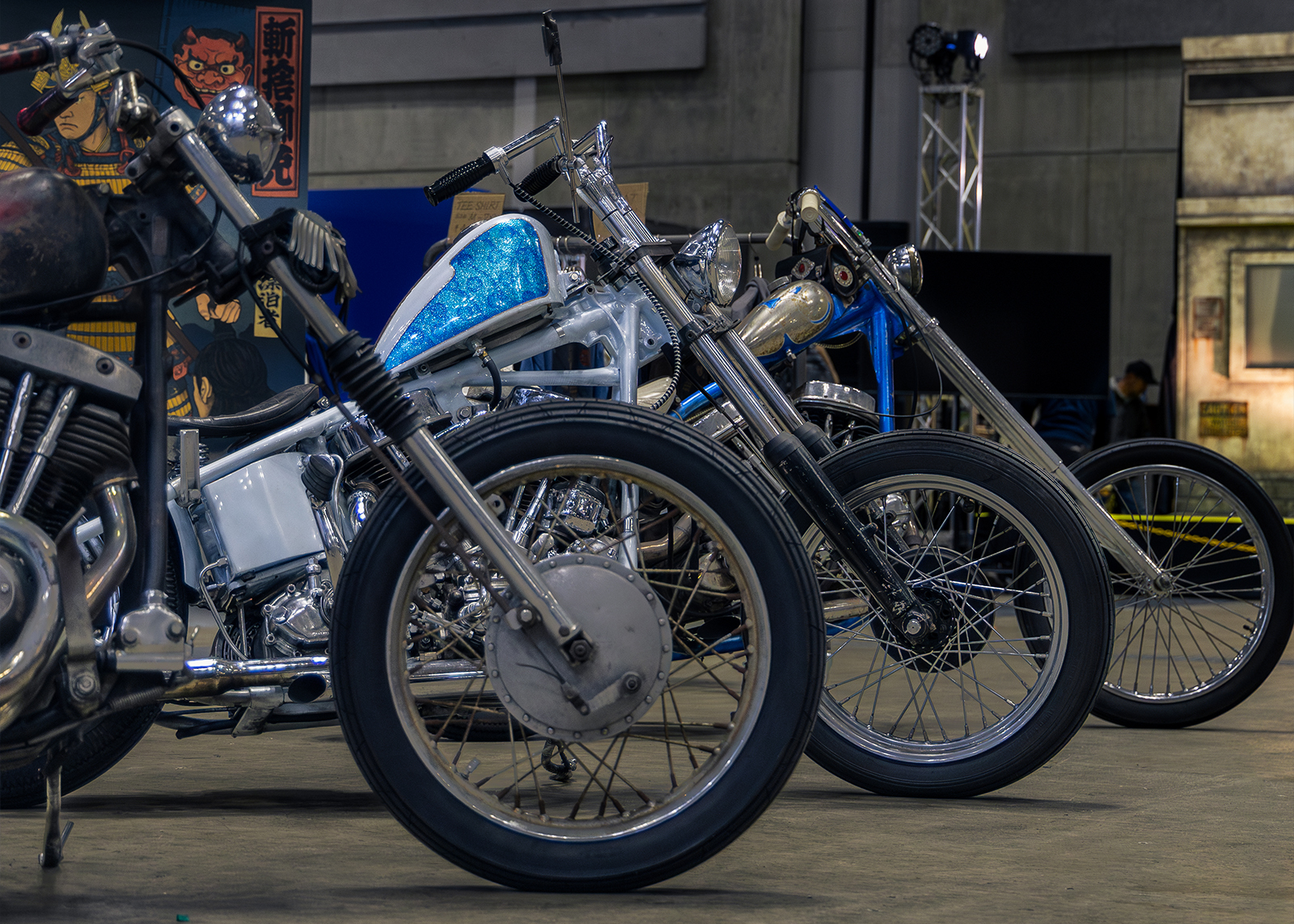 A row of custom choppers is lined up in a warehouse space at the Mooneyes Yokohama Rod Custom Show