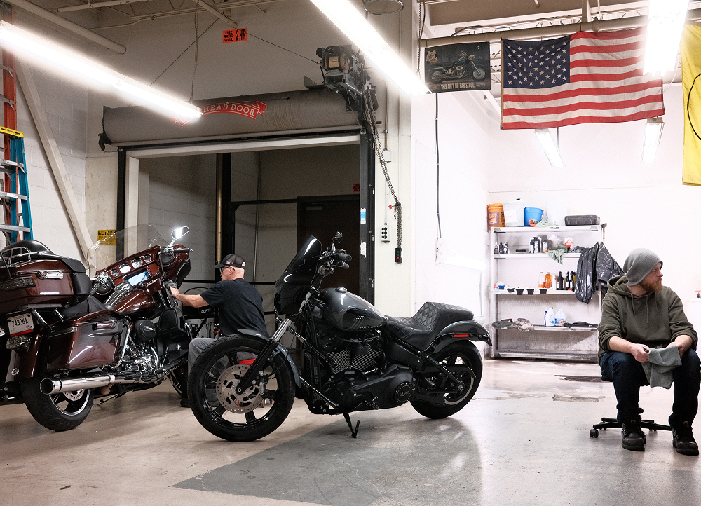 Motorcycle parked inside a service garage while a technician works nearby, with tools and equipment in the background
