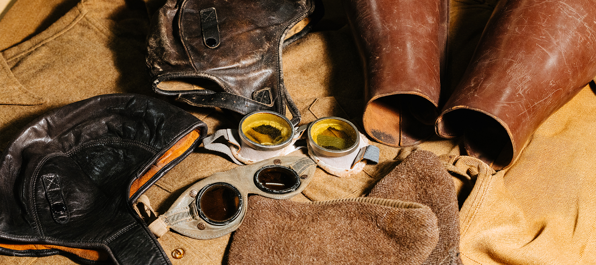  A collection of vintage motorcycle gear including leather helmets, goggles, boots, and wool clothing.
